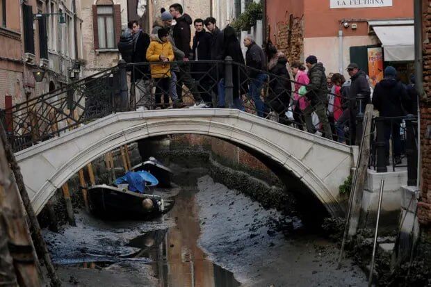 Туристи переходять міст через помітно порожній канал під час сильного відливу у Венеції, Італія