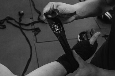 Человек обматывает руку боксерским бинтом перед тренировкой