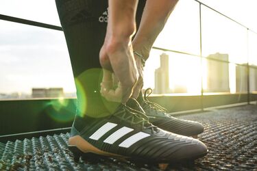 Футболист завязывает шнурки на бутсах перед тренировкой на фоне городского заката