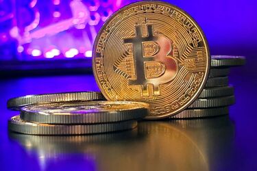 Золотые биткойн-монеты на фоне фиолетовой подсветки