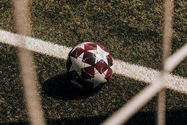 Футбольный мяч на поле возле линии ворот, снятый через сетку