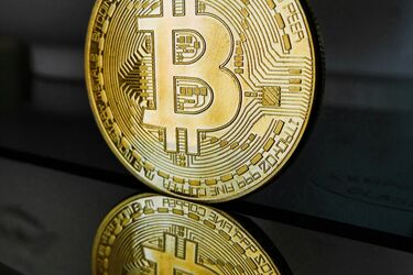 Золота монета з логотипом біткоїна та її відображення на дзеркальній поверхні