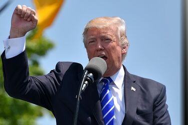 Дональд Трамп выступает с речью на открытом воздухе, рядом развивается флаг США