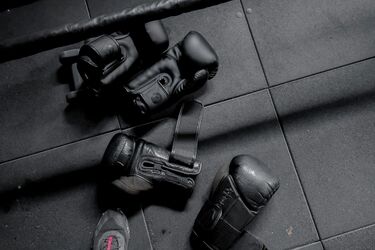 Черные боксерские перчатки лежат на полу у ринга рядом с ногами спортсмена в кроссовках