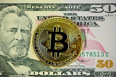 Золота монета з символом Bitcoin на фоні 50-доларової купюри США