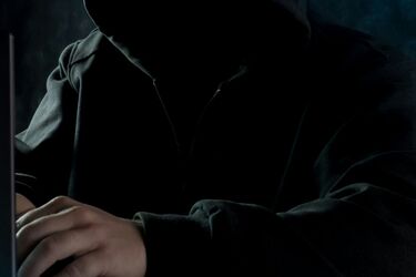 Особа в капюшоні працює за ноутбуком у темному приміщенні